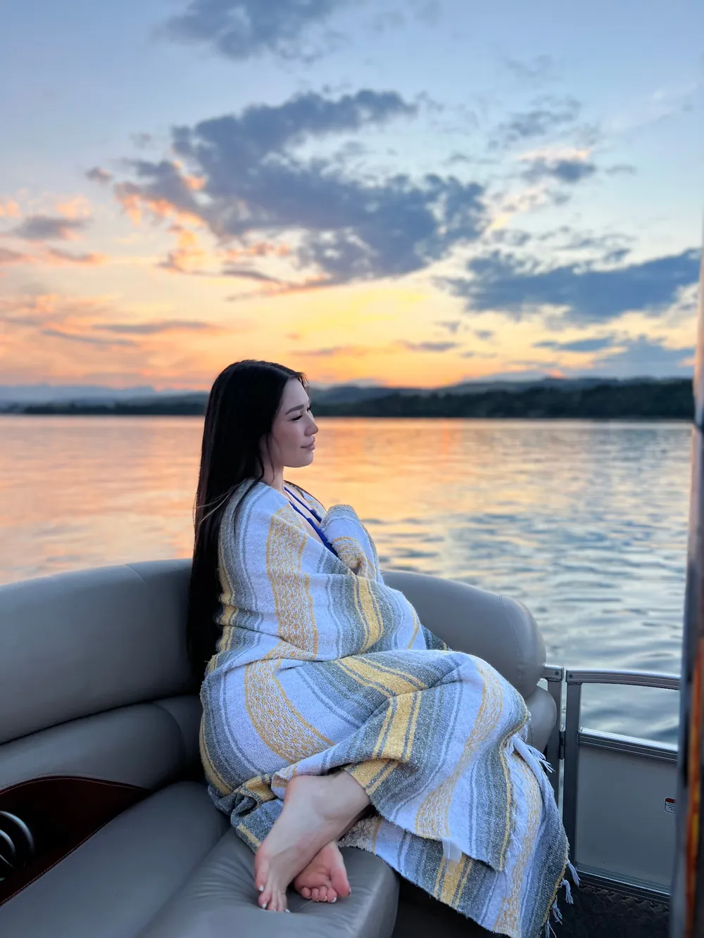 A guest wrapped in a blanket watching the sunset from the boat
